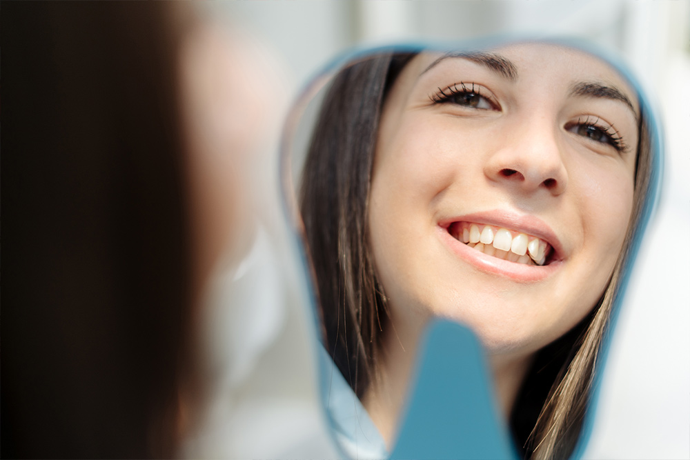 Ragazza che si guarda allo specchio dopo una sessione di sbiancamento dentale presso lo Studio Medico Dentistico Santa Apollonia
